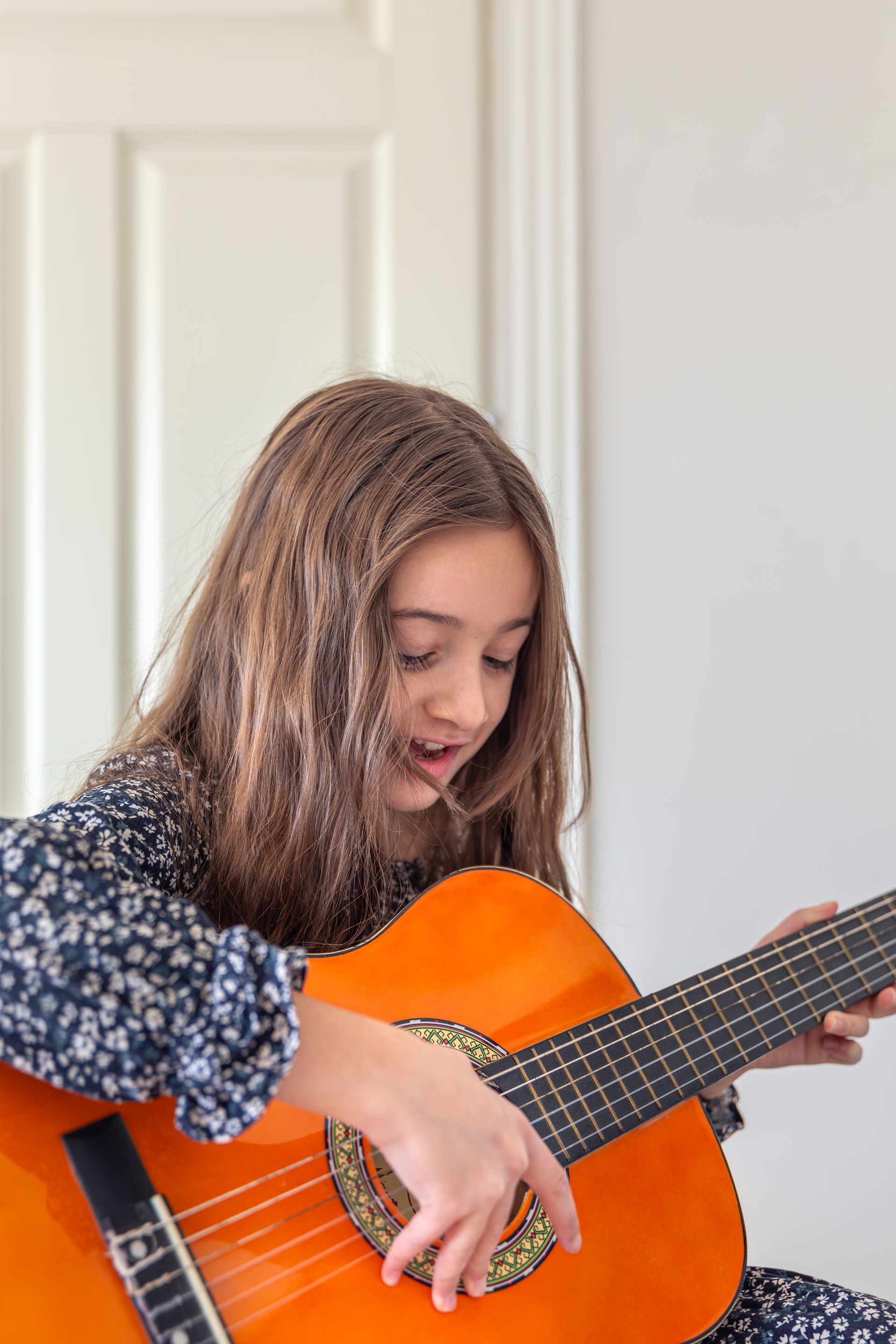 A young girl is playing an orange guitar in a room.