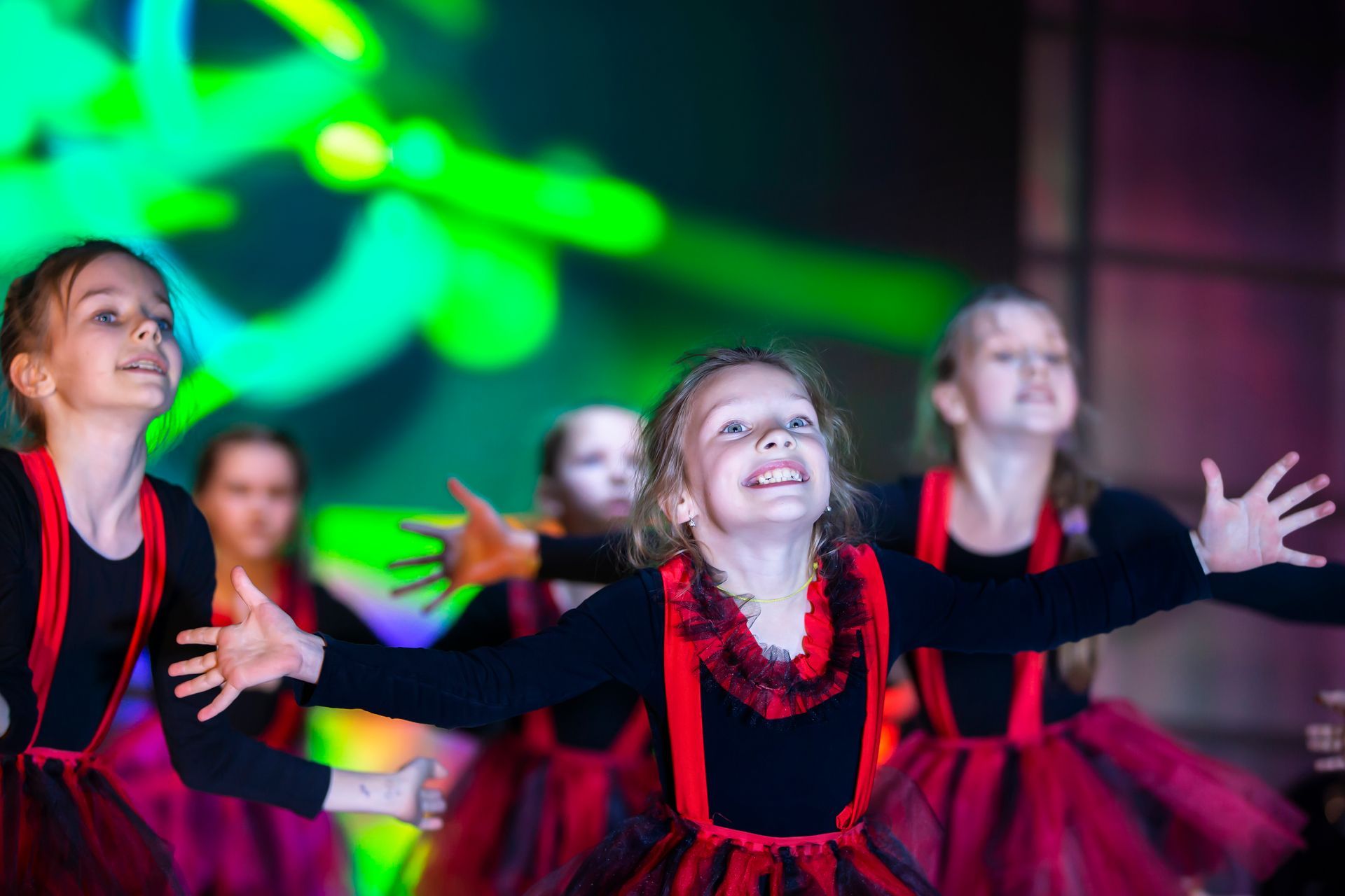 Children in black and red costumes performing a dance on stage with colorful lights