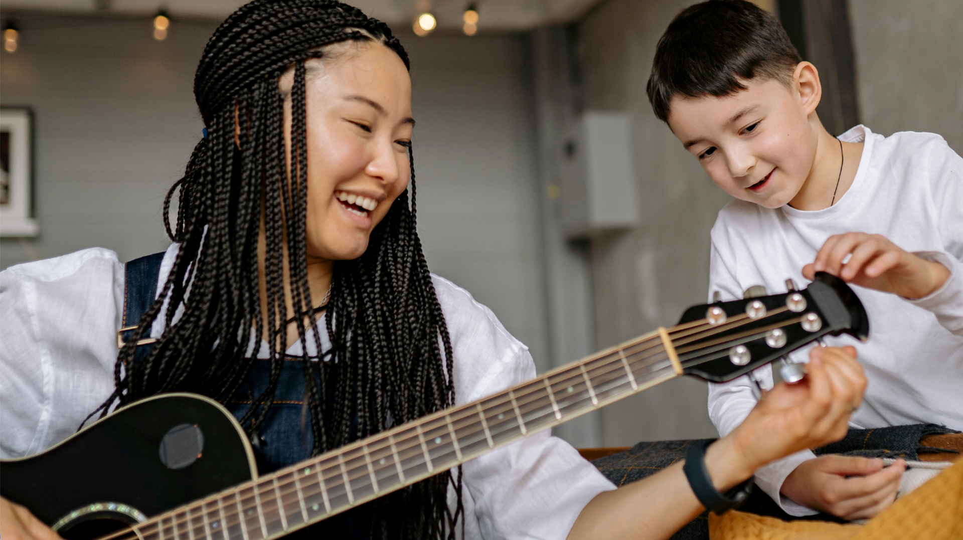 Man in a wheelchair playing guitar while a woman stands beside him in a bright living room