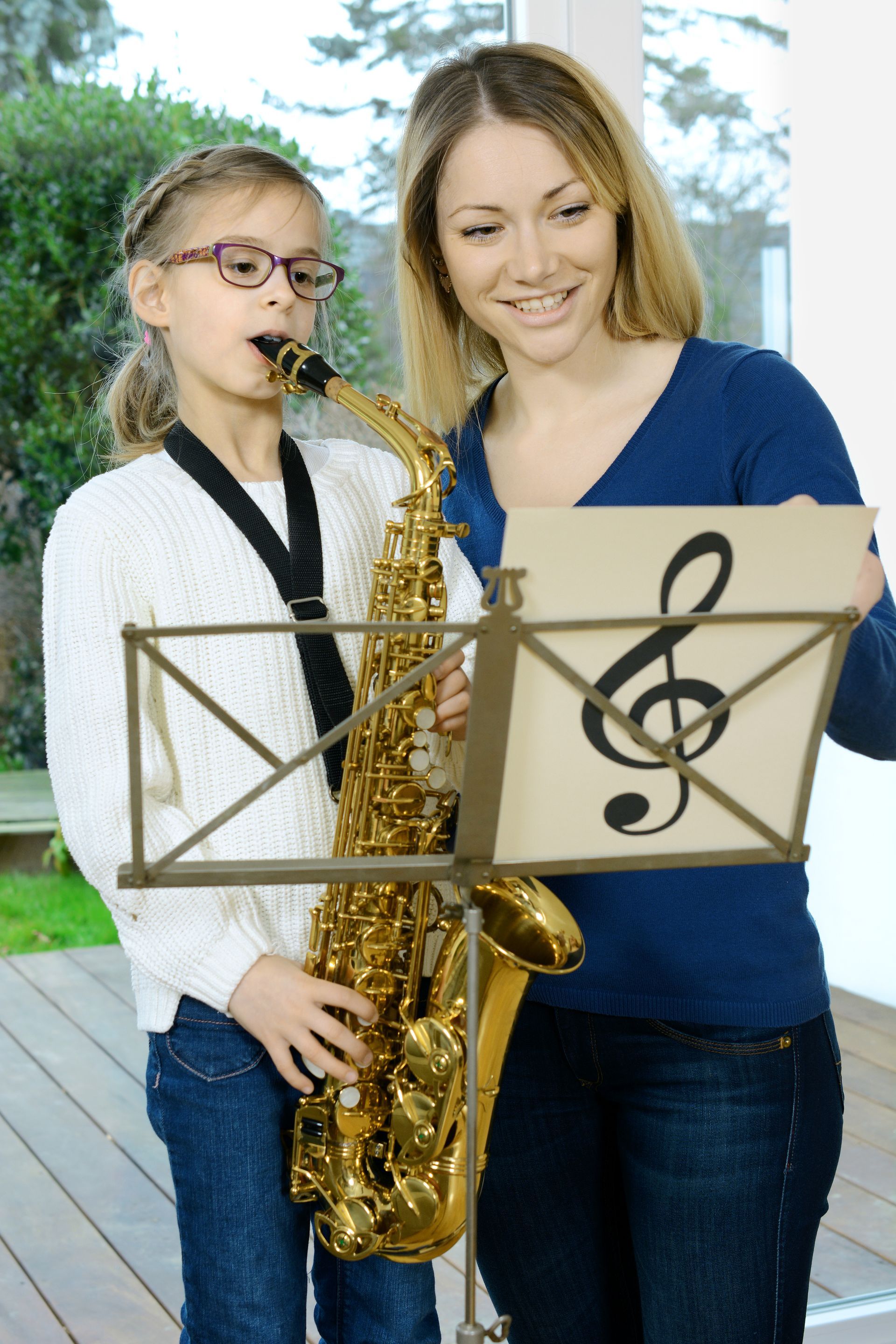 Woman and girl playing saxophone; woman smiles at sheet music.