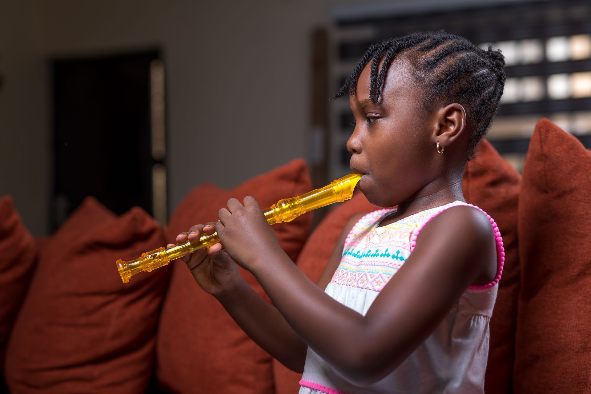 A little girl is playing a flute in a living room.