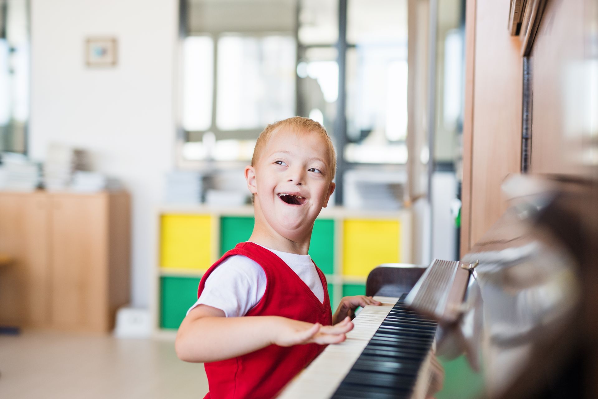 A young boy with down syndrome is playing a piano and smiling.