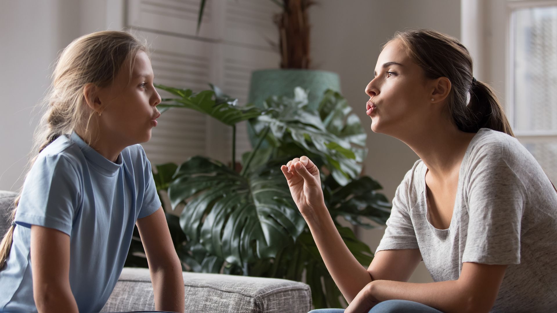 A mother and daughter are sitting on a couch talking to each other.