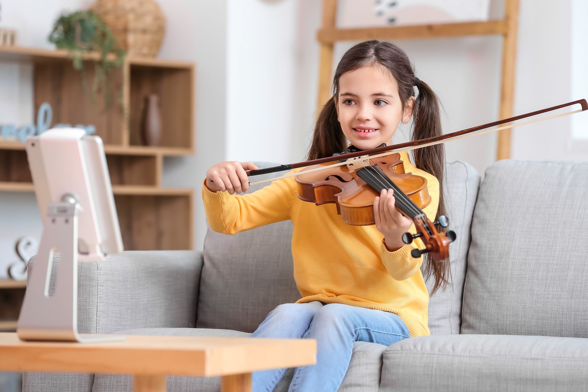 A young girl is sitting on a couch playing a violin.