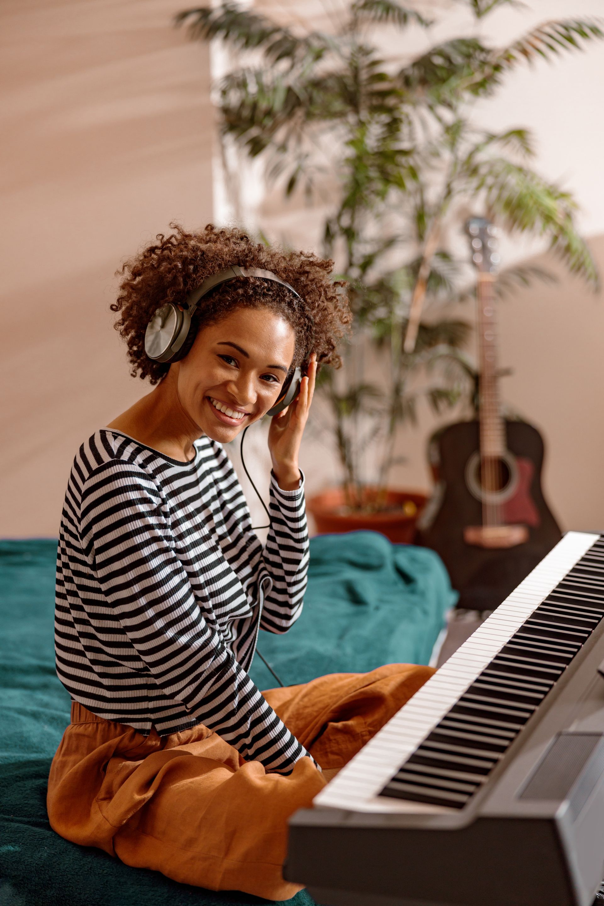 A woman is sitting on a bed playing a piano and listening to music.
