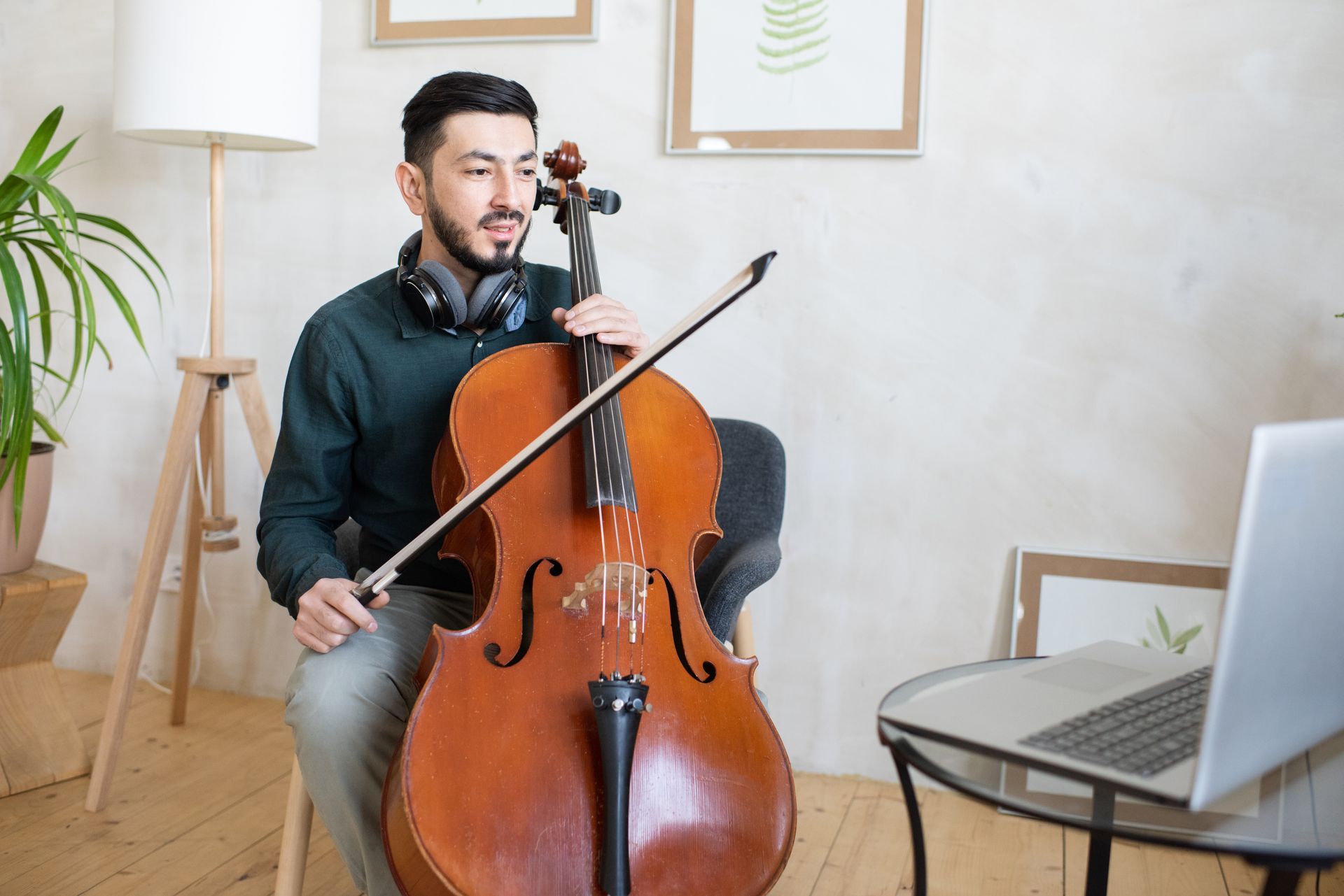 A man is playing a cello in front of a laptop computer.