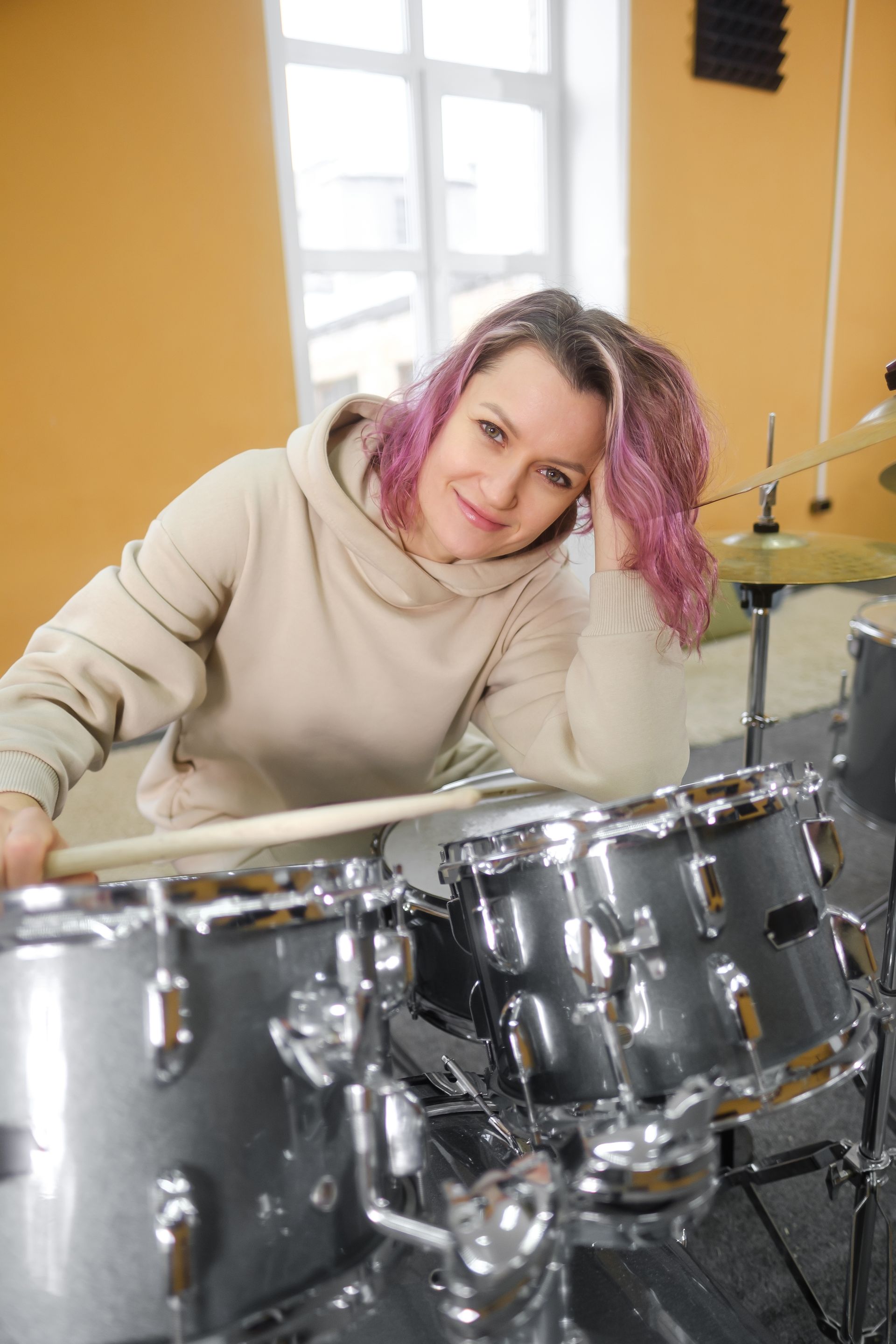 A woman with pink hair is sitting in front of a drum set.