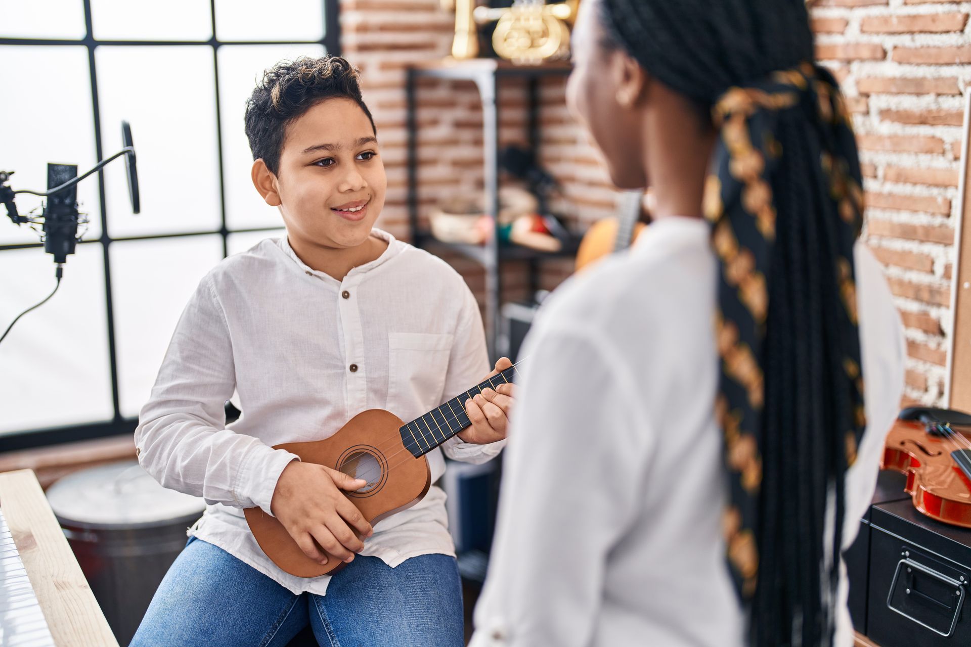 A boy is playing a ukulele and talking to a woman.