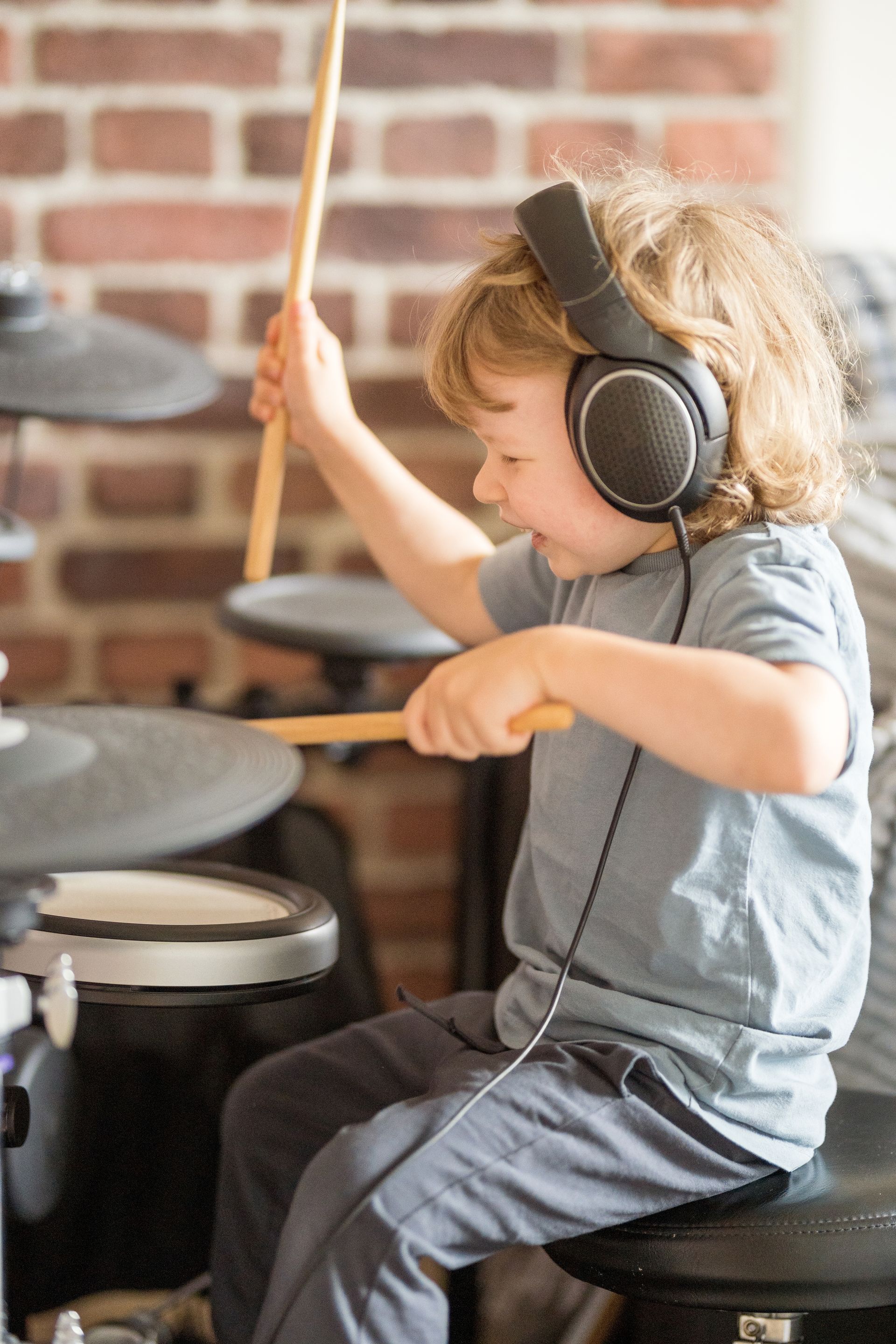 A young boy wearing headphones is playing drums.
