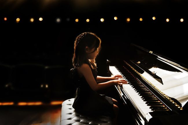 Girl playing piano, lit by stage lights.