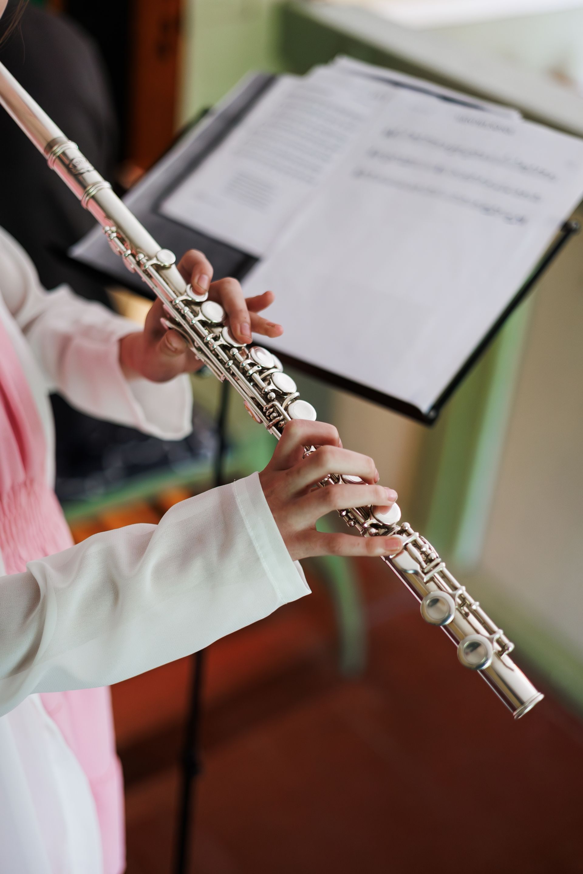 Person playing a silver flute, reading sheet music on a stand.