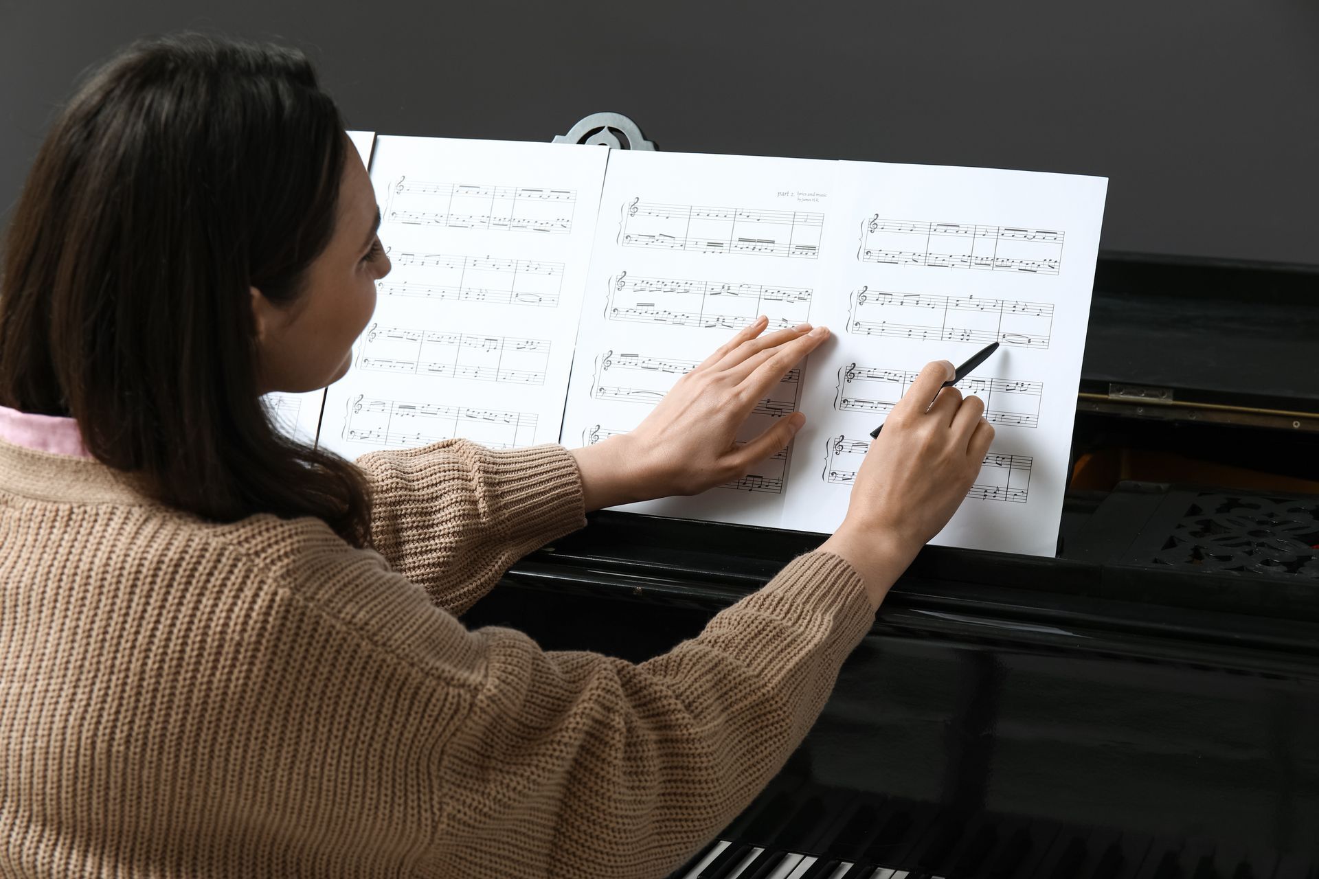 Woman with pen, studying musical score on a piano.