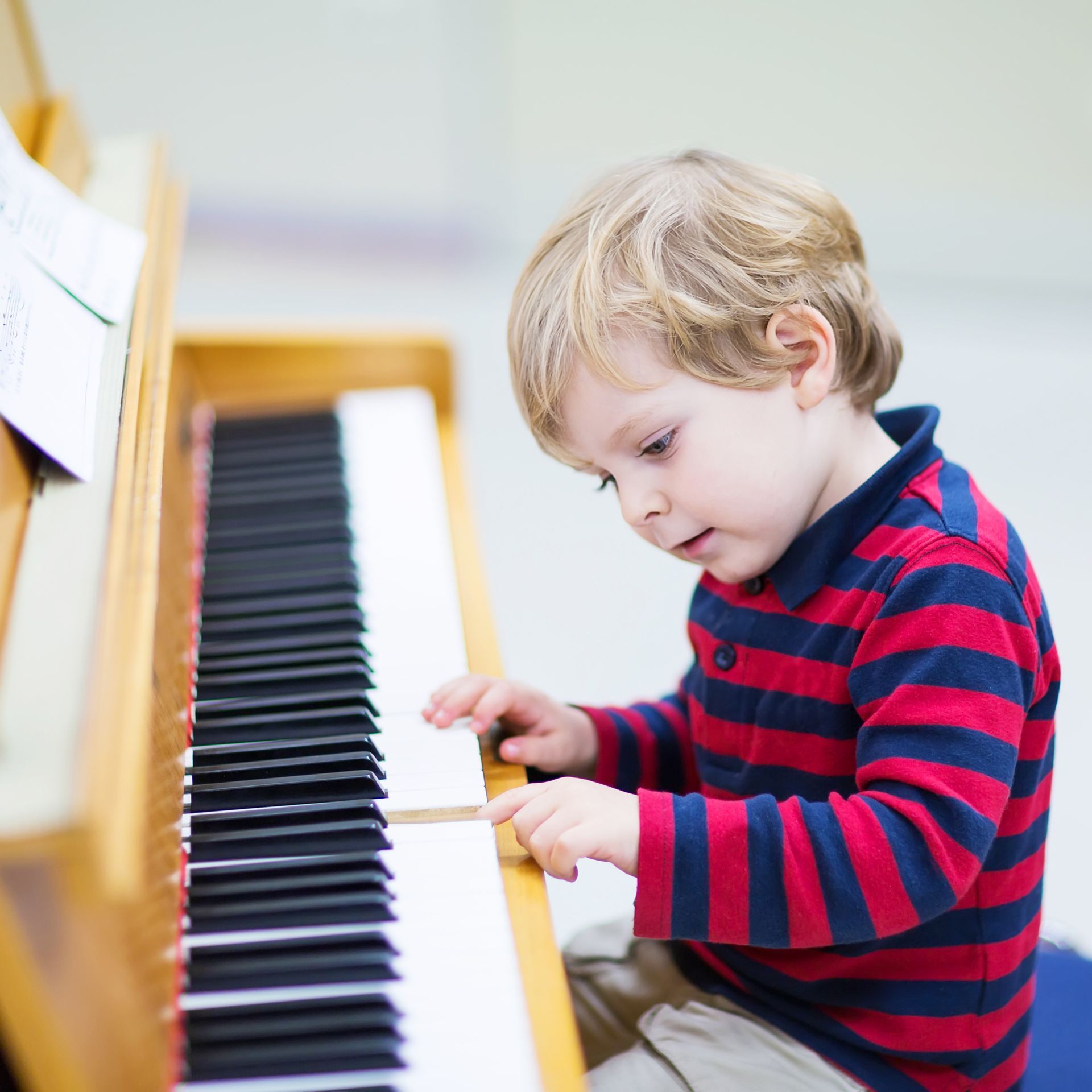 A young boy in a red and blue striped shirt is playing a piano