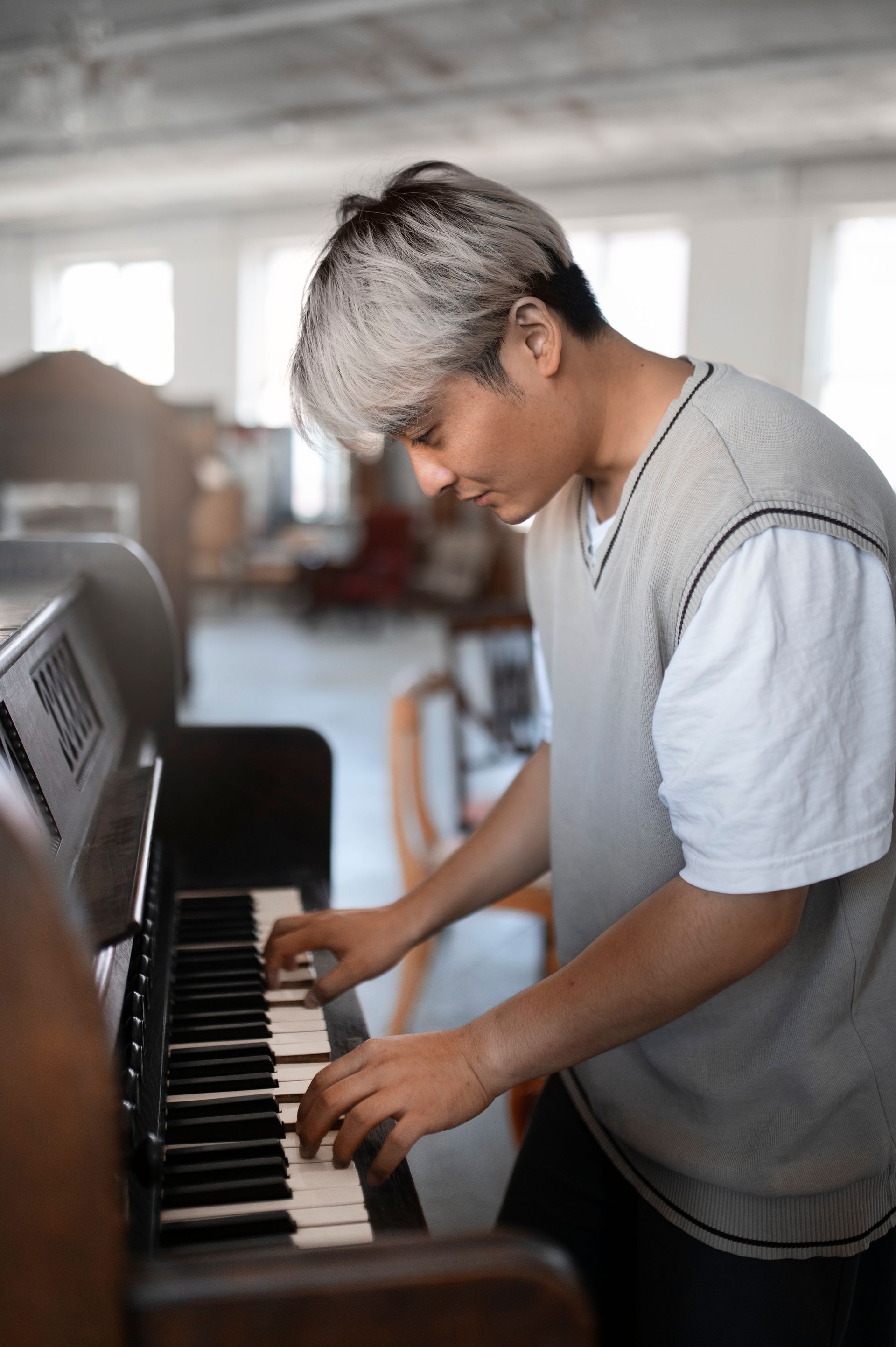 Person playing a black piano in a bright room, looking down at the keys.