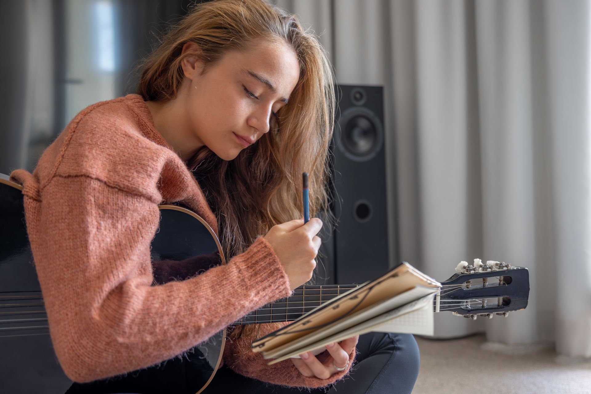 Person writing in a notebook while sitting by a speaker in a bright room