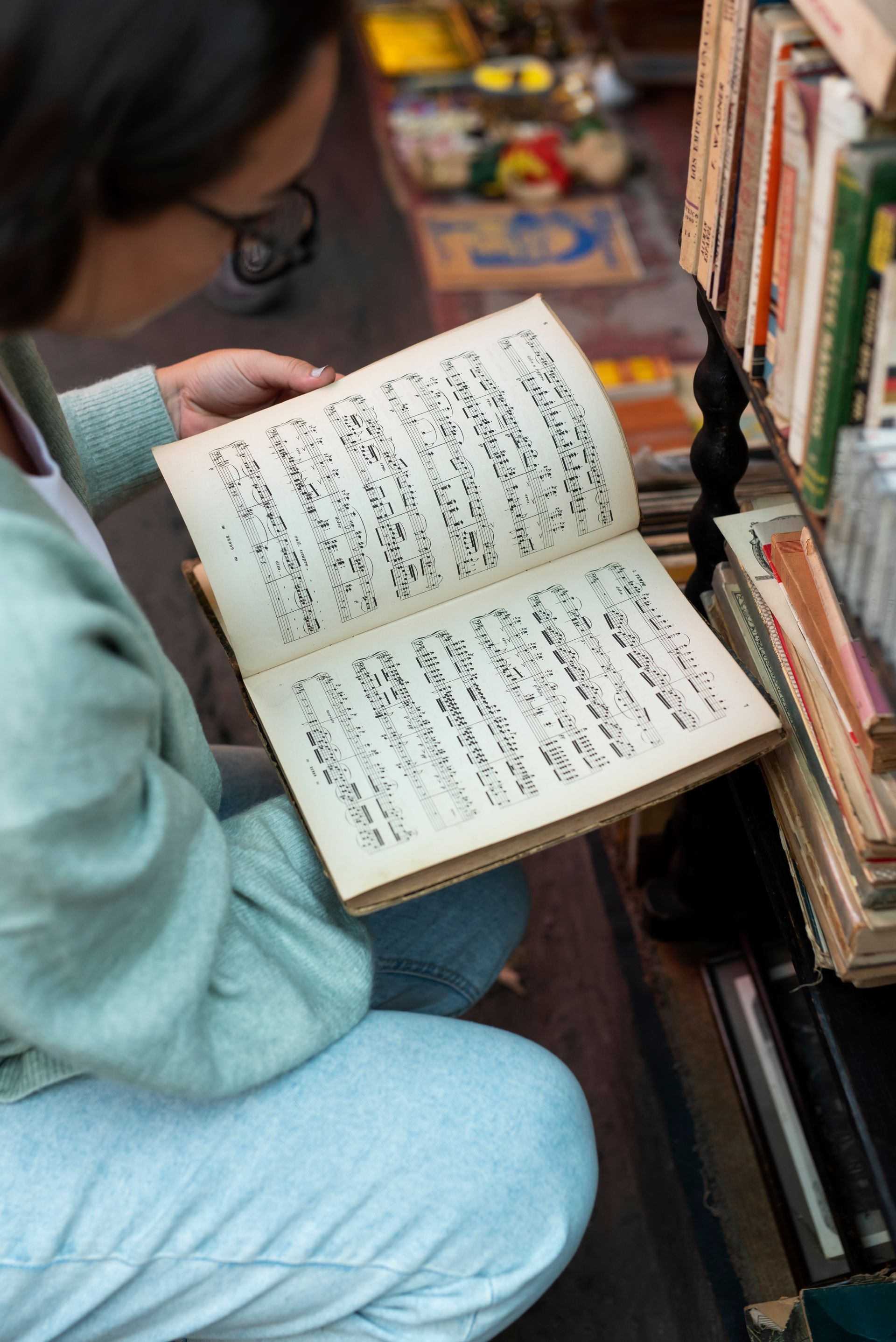 A woman is kneeling down reading a book in a library.