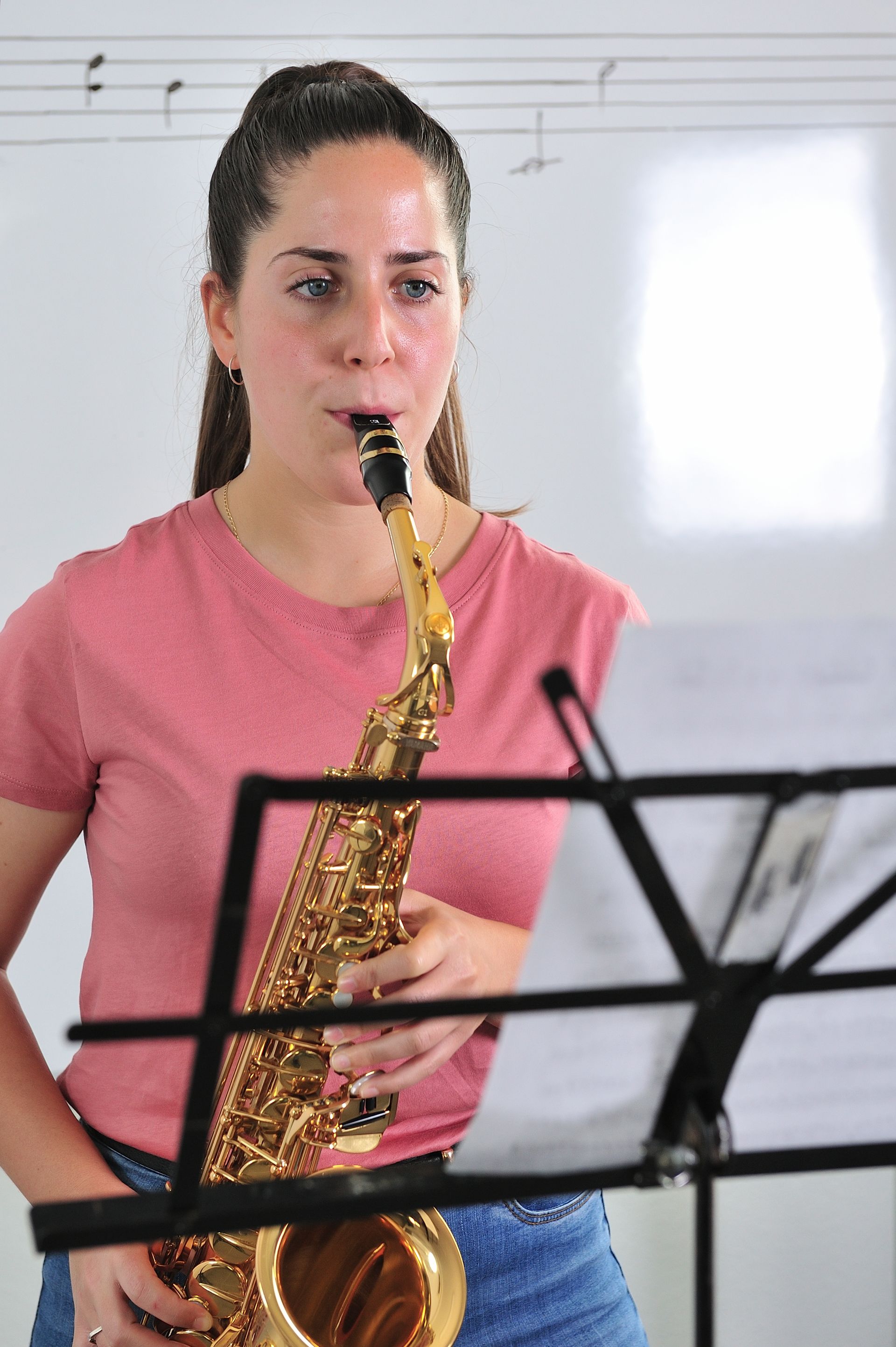 A woman is playing a saxophone in front of a music stand.