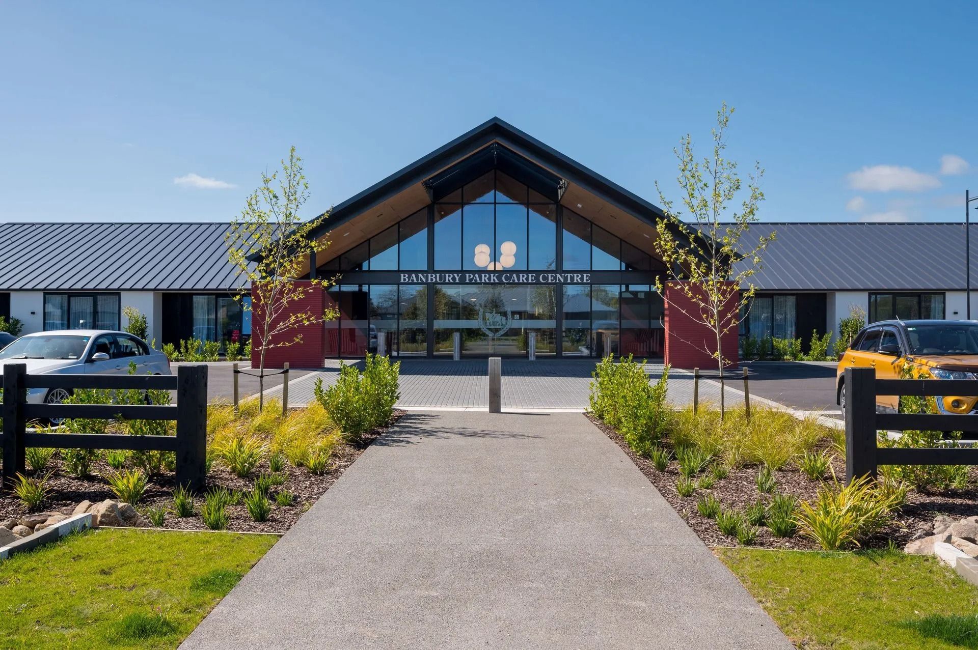 A modern building with a peaked roof entrance, glass doors, and a pathway leading to it.