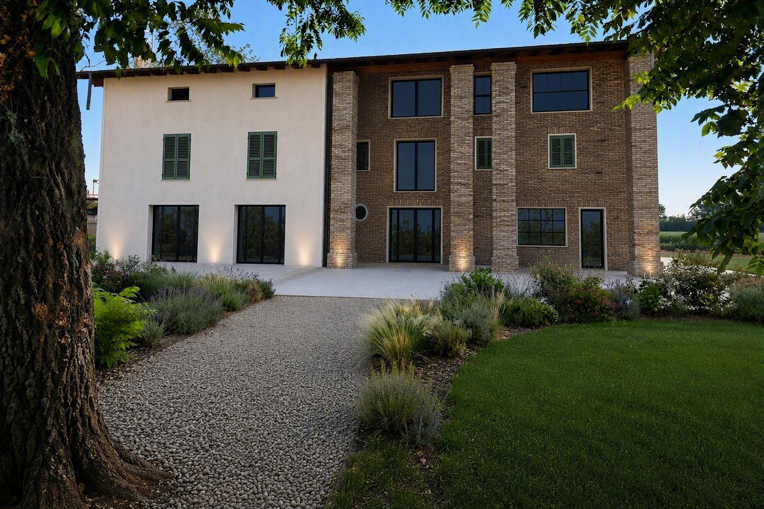 Casa moderna a due piani con facciata in stucco bianco e mattoni, vialetto di ghiaia e prato curato sotto gli alberi.