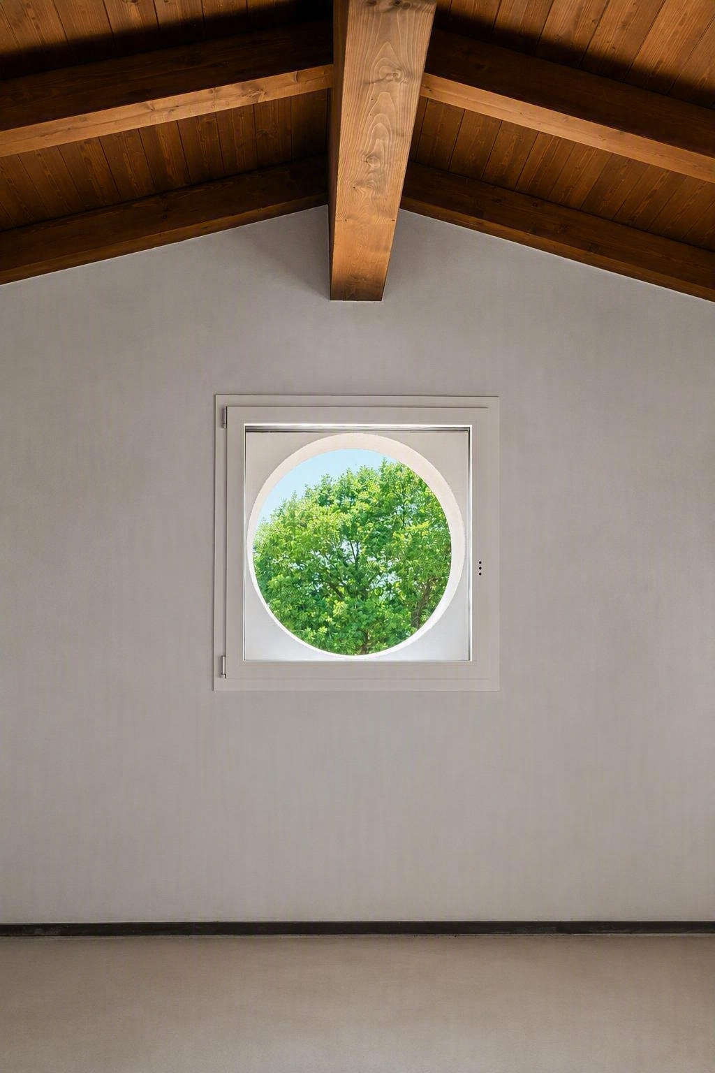 Interno della mansarda con travi in legno a vista e una piccola finestra rotonda che mostra gli alberi verdi all'esterno.