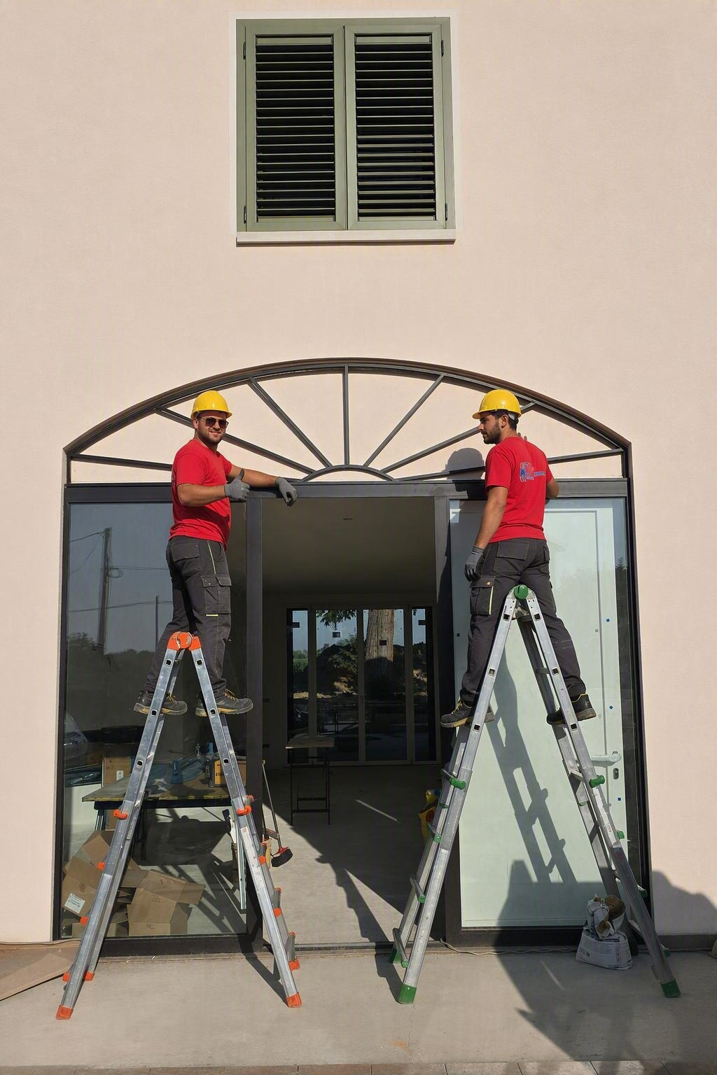 Due operai su delle scale installano una struttura metallica ad arco sopra l'ingresso di un edificio.