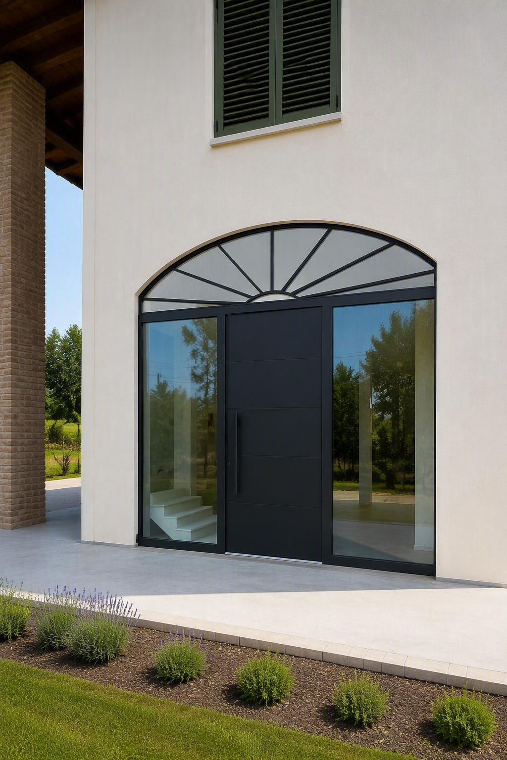 Ingresso di un edificio moderno con porta ad arco scura, vetrate laterali e facciata bianca.