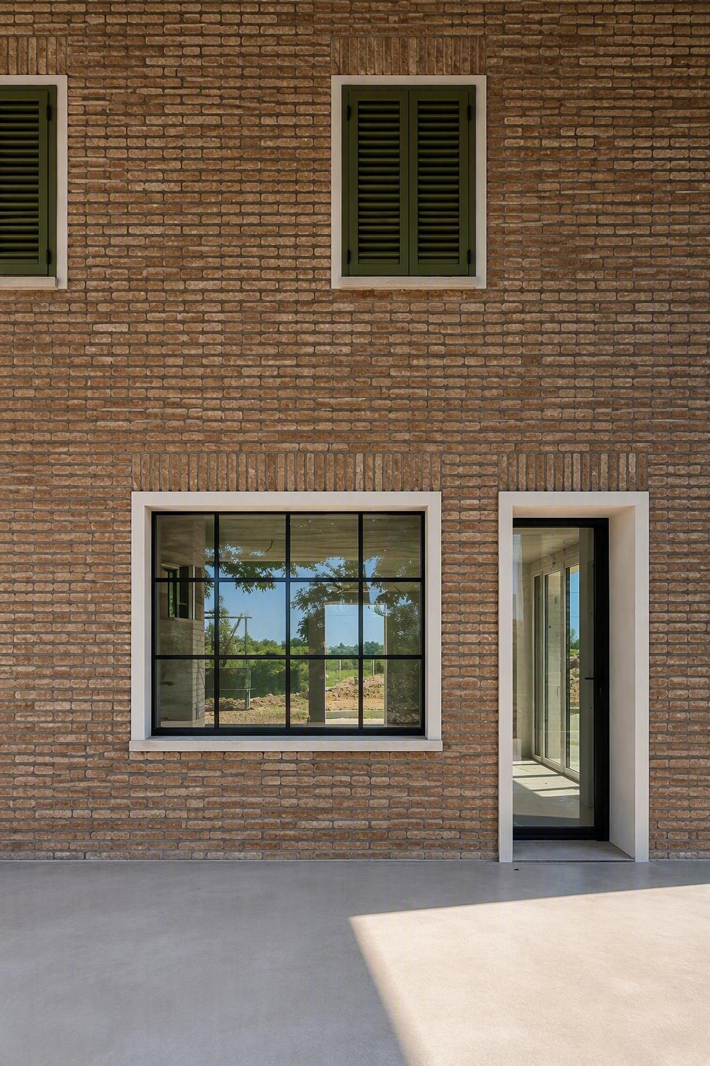 Esterno di un edificio in mattoni con finestre, una porta e un patio in cemento antistante.