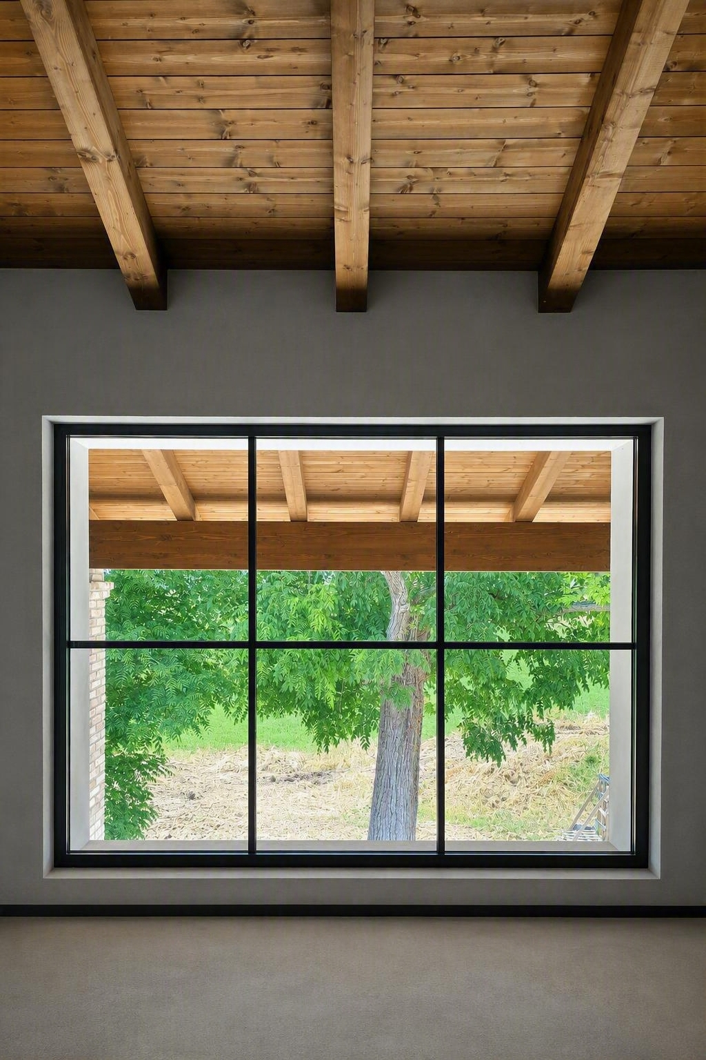 Soffitto in legno e ampia finestra con vista su alberi verdi e una terrazza esterna.