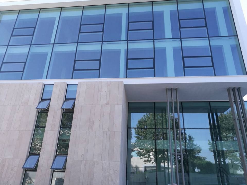 Facciata moderna di un edificio per uffici con finestre in vetro blu e pannelli in pietra beige.