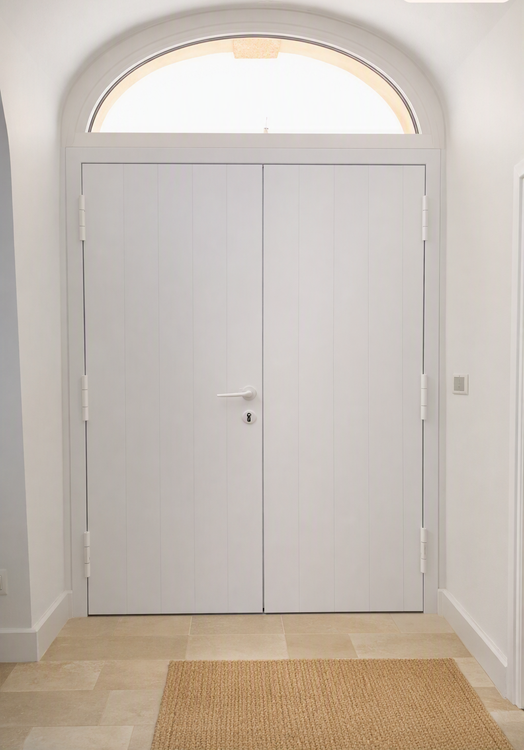 Doppie porte d'ingresso bianche sotto una finestra ad arco in un corridoio luminoso con pavimento beige e un piccolo tappeto