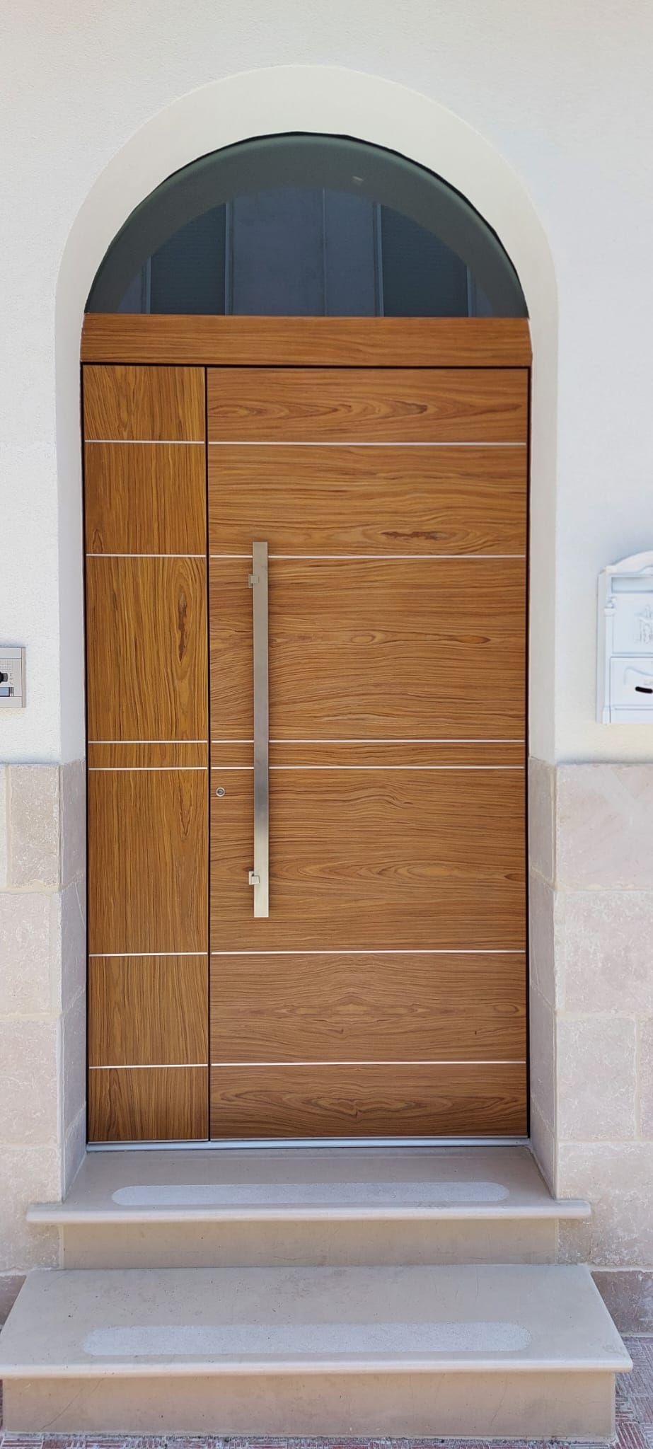 Porta d'ingresso in legno con finestra ad arco, incorniciata da un ingresso e scalini in pietra.