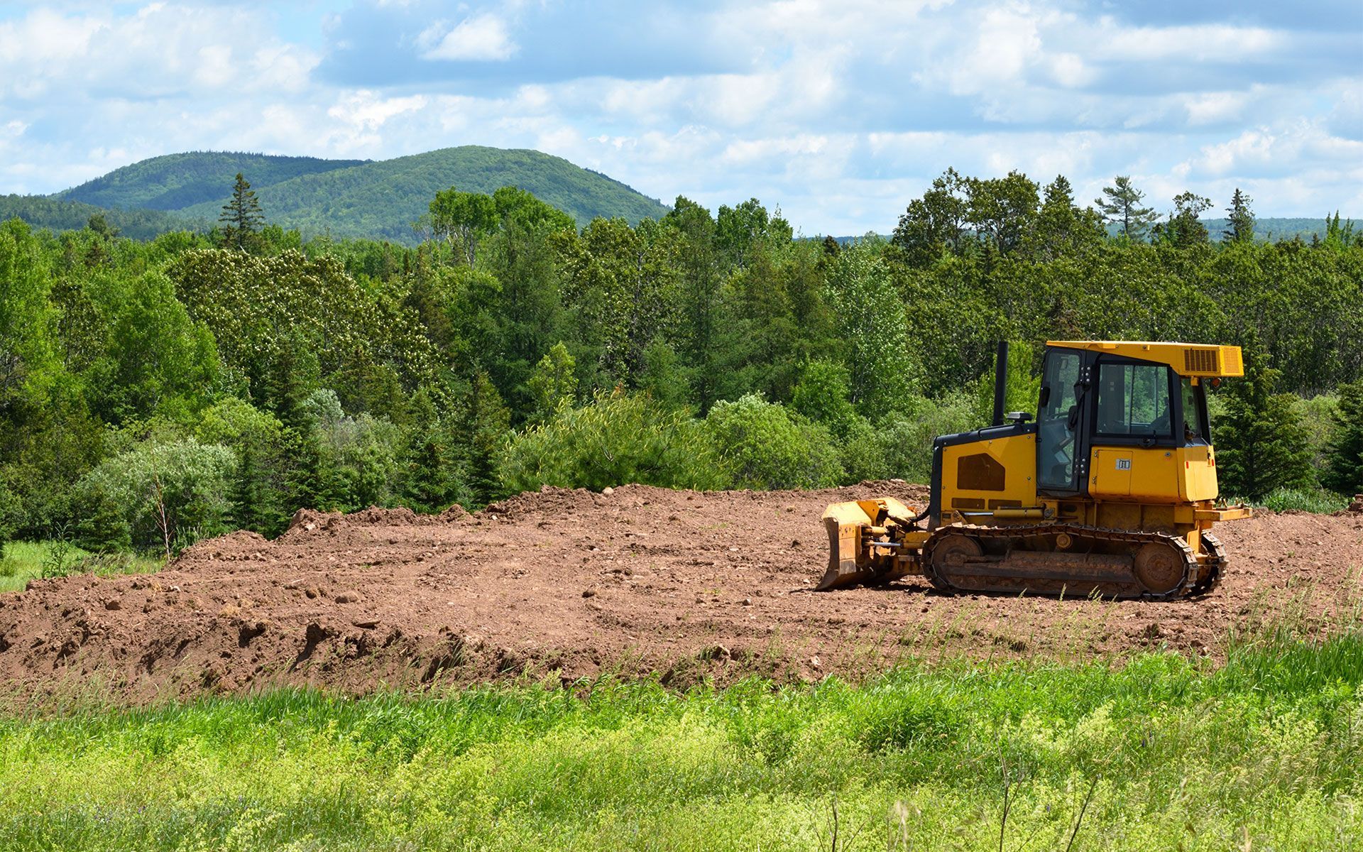 A bulldozer is plowing a field with mountains in the background.
