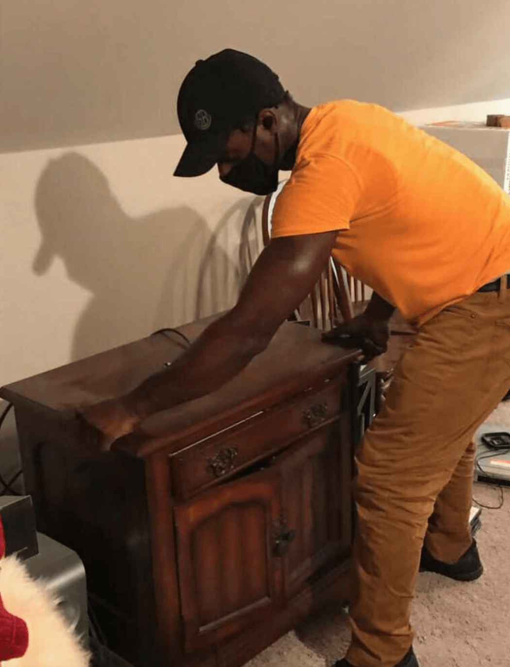 A man wearing a mask is bending over a wooden dresser.