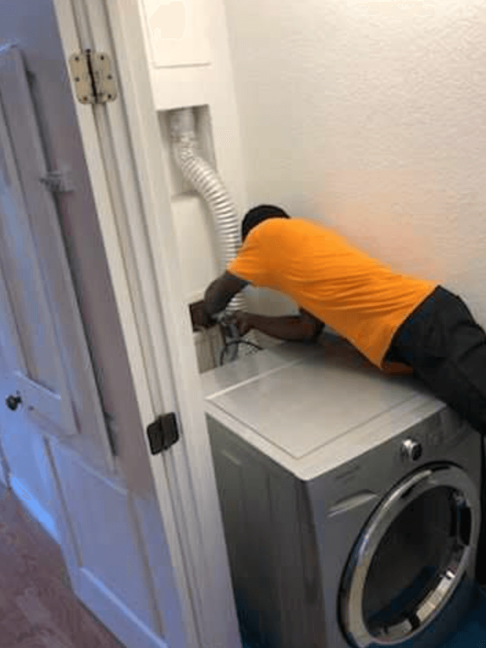 A man is working on a washer and dryer in a laundry room.