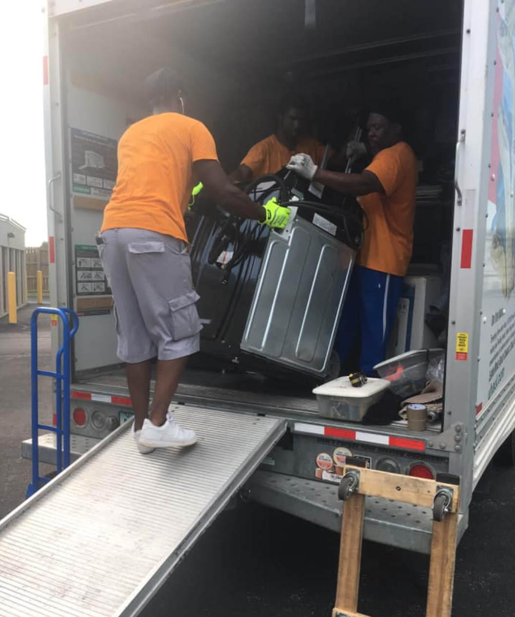 A man in an orange shirt is loading a fridge into a truck