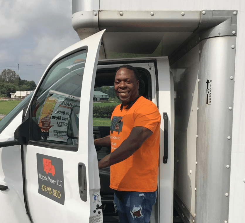 A man in an orange shirt is getting out of a white truck