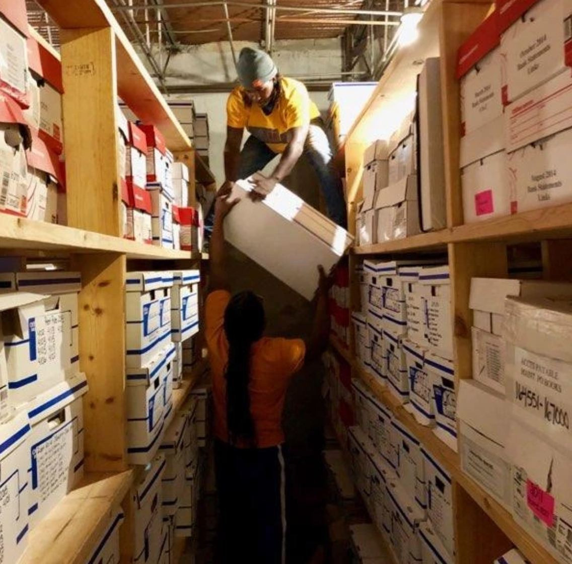 A man in a yellow shirt is carrying a box in a warehouse