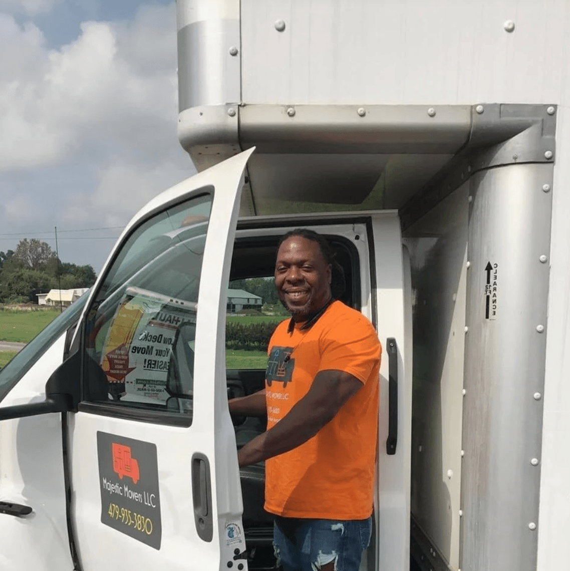 A man in an orange shirt is getting out of a moving truck