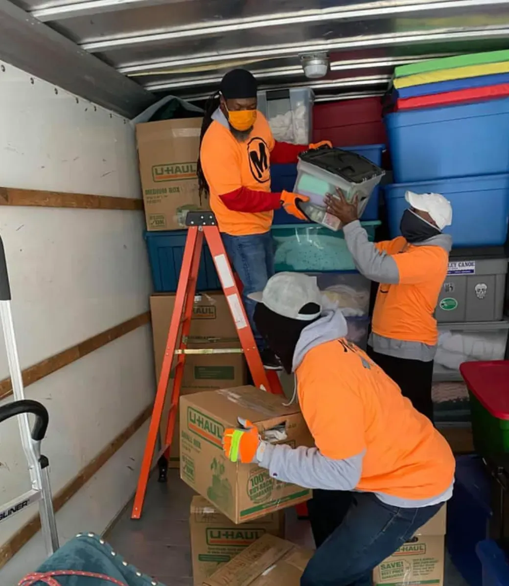 Two men wearing masks are loading boxes into a truck