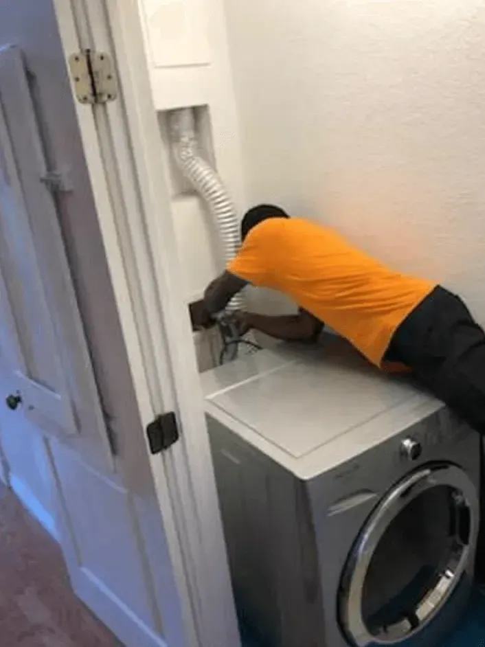 A man is working on a washing machine in a laundry room.
