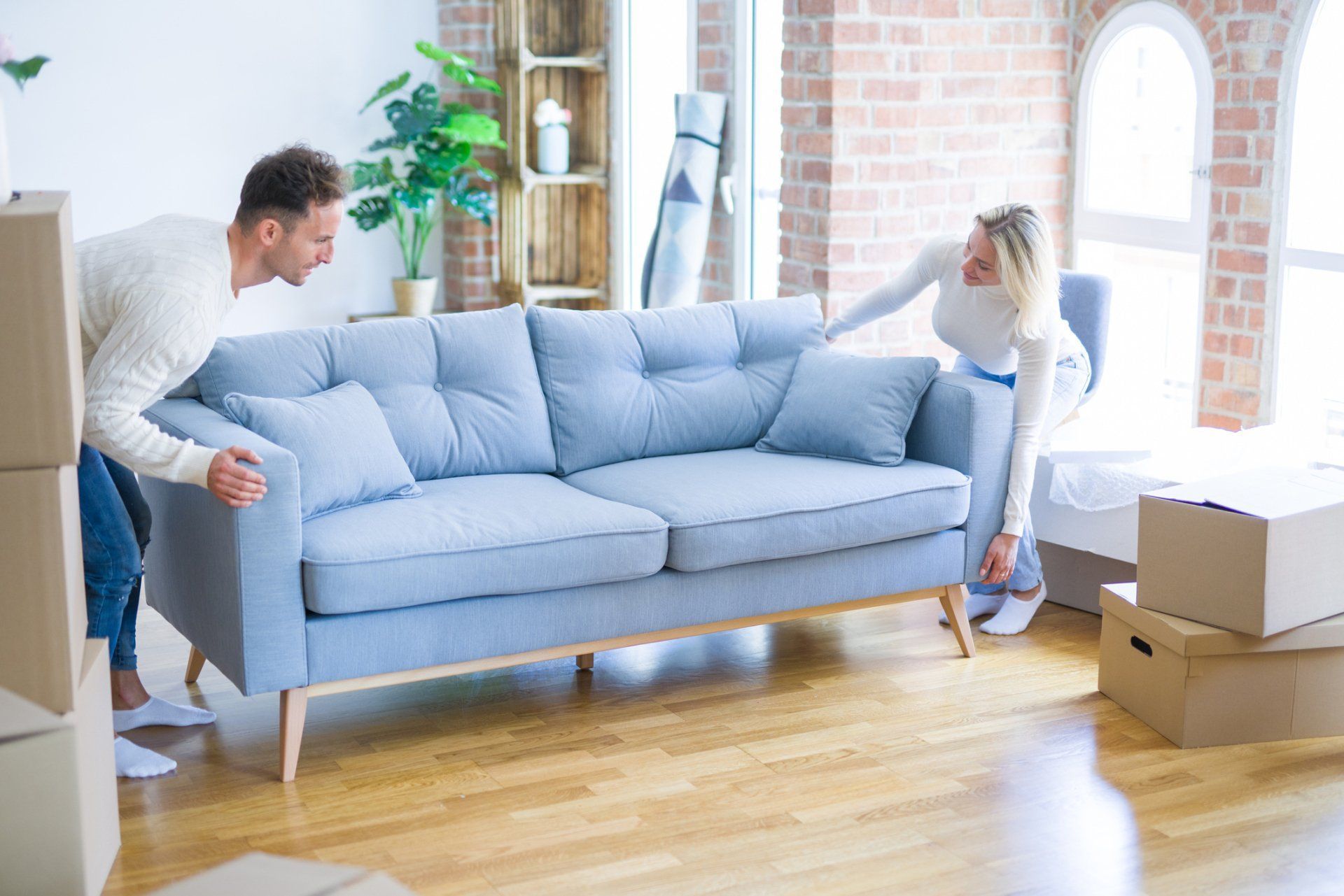 A man and a woman are moving a couch in a living room.