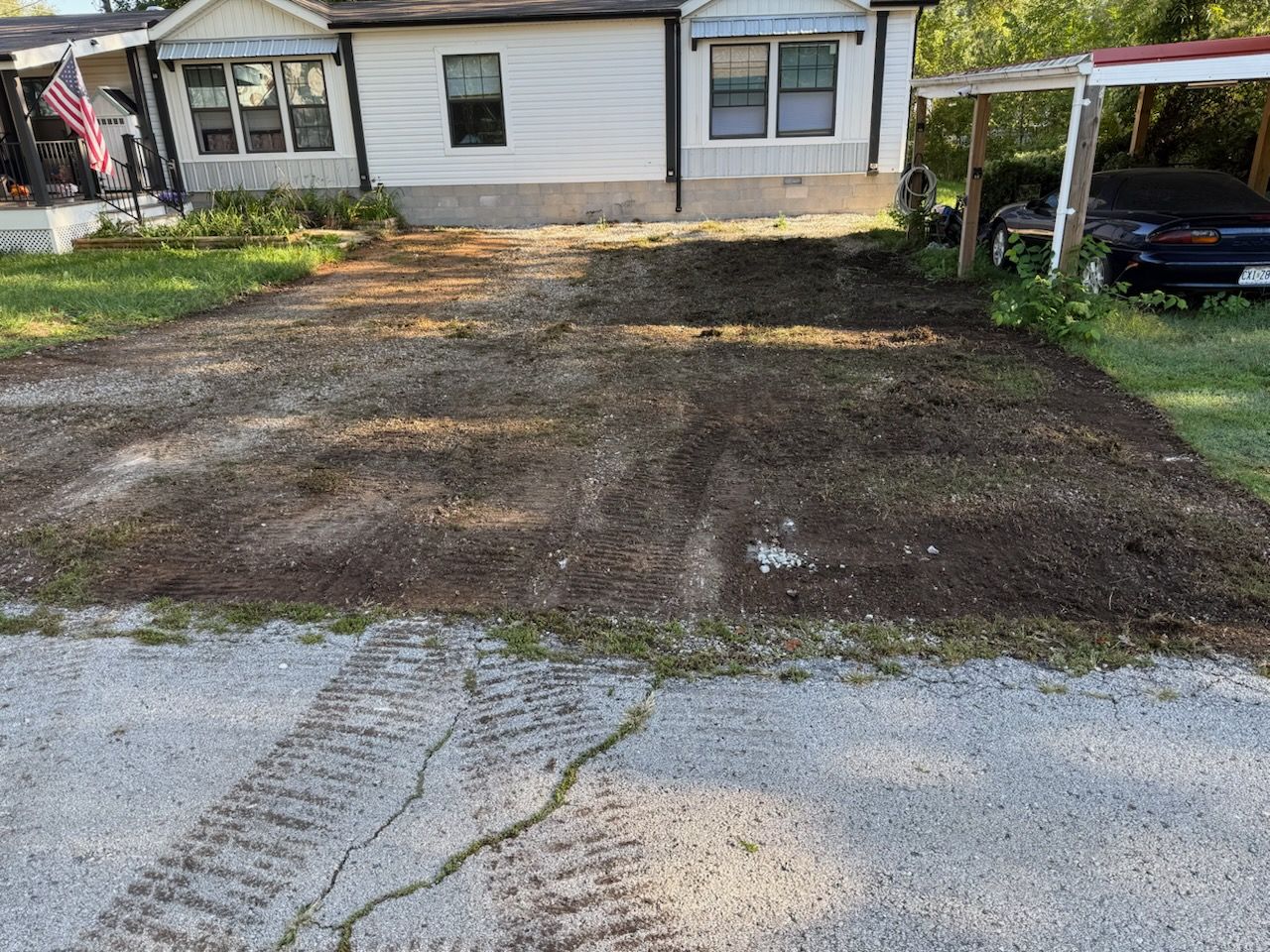 A gravel driveway leading to a white house with a car parked under a carport.