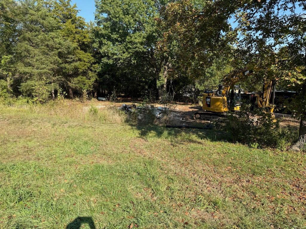 Yellow excavator on construction site clearing brush and trees.