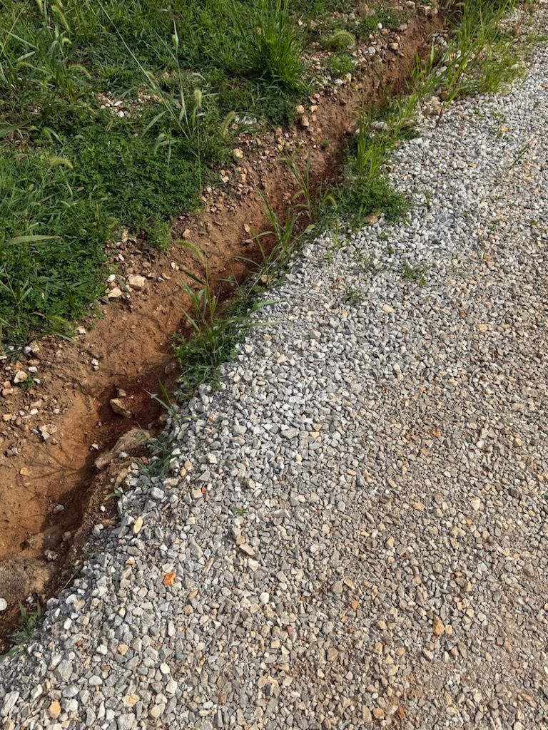 Gravel path next to a grass verge with a small, dirt ditch running along the edge.