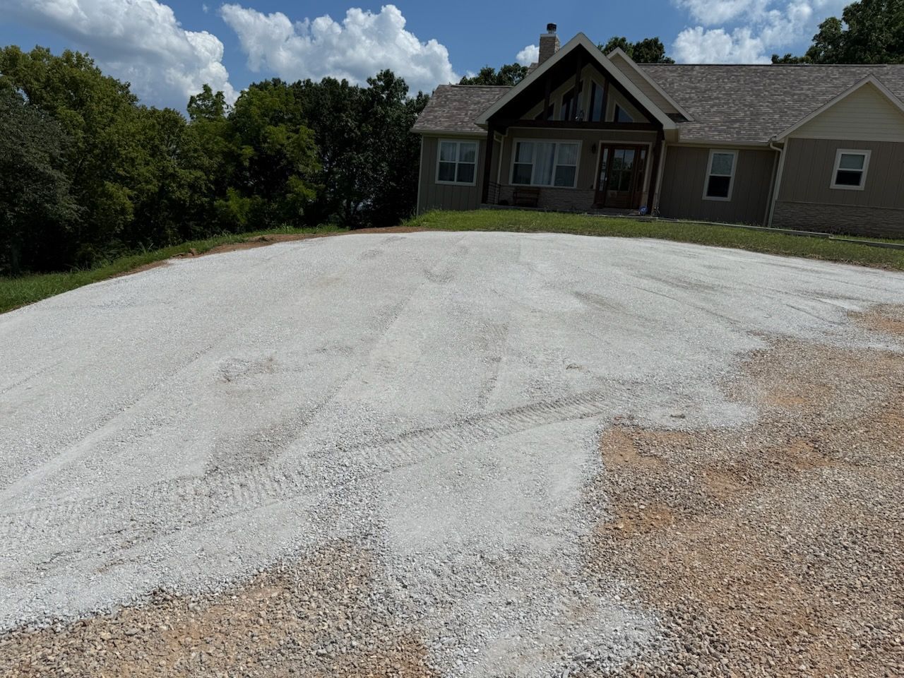 Gravel driveway in front of a tan house with a dark brown front door and a green lawn.