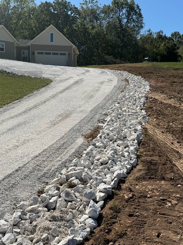 Gravel driveway with a row of large white rocks along the right edge. A house with a garage is in the background.