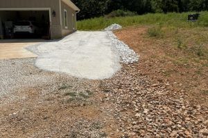 Driveway with gravel border next to a beige house, with a partially poured concrete area.