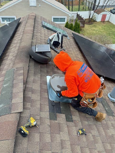 Roofer in orange hoodie working on a rooftop with tools, surrounded by solar panels, in a suburban setting.