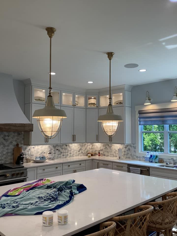 Bright white kitchen with large island, pendant lights, tiled backsplash, and a window above the sink.