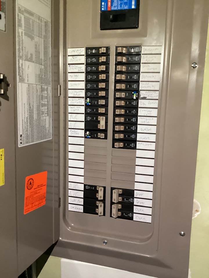Open electrical breaker panel with rows of labeled switches and one open door.